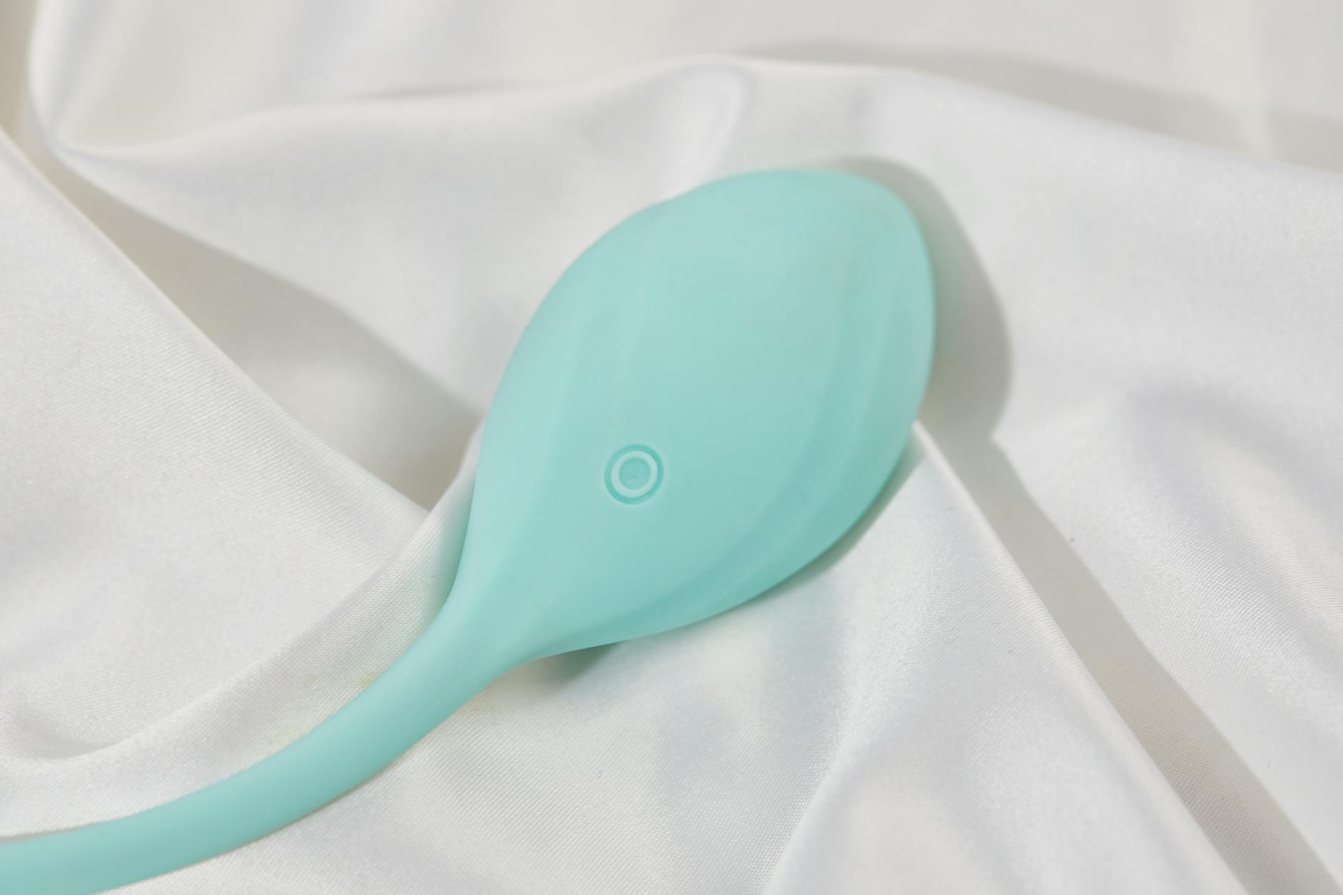 A teal lemon clitoral vibrator resting on soft white silk fabric