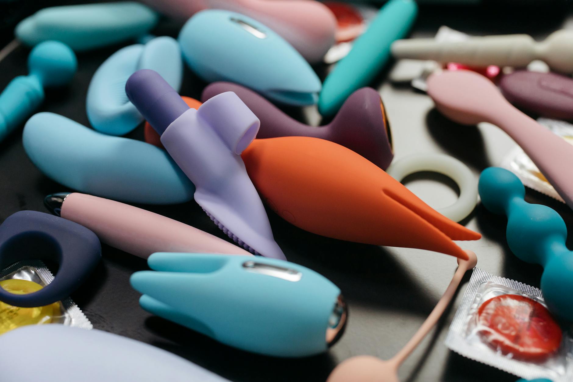 Zwei Hände halten rosa und blaue Silikon-Vibratoren vor einem pastellfarbenen Hintergrund