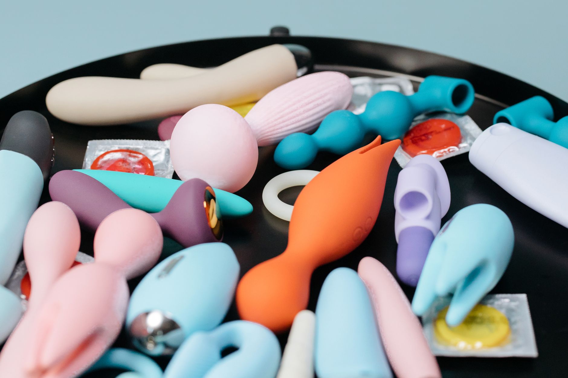 Eine Frau mit Brille hält einen blauen und rosa Vibrator nachdenklich in den Händen