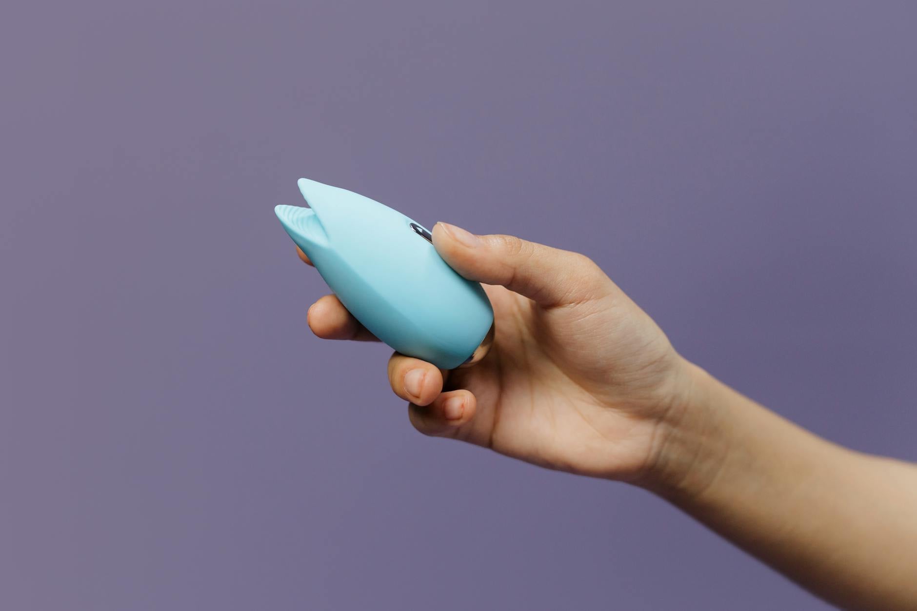 Ein blauer Silikonvibrator in der Hand vor solidem lila Hintergrund, fördert Selbstliebe und Sexualität
