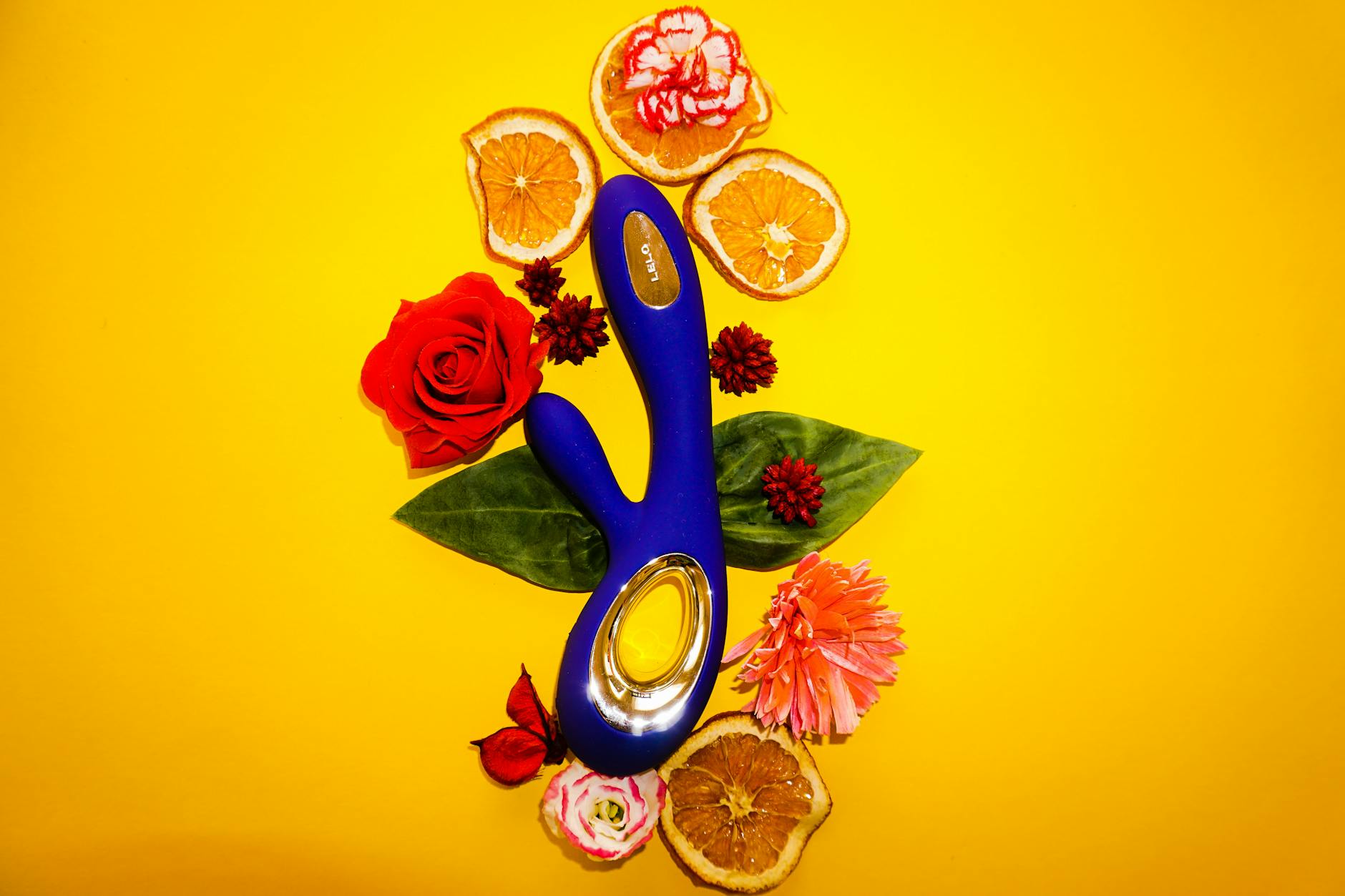 Lemon vibrator surrounded by flowers and citrus on a bright yellow surface