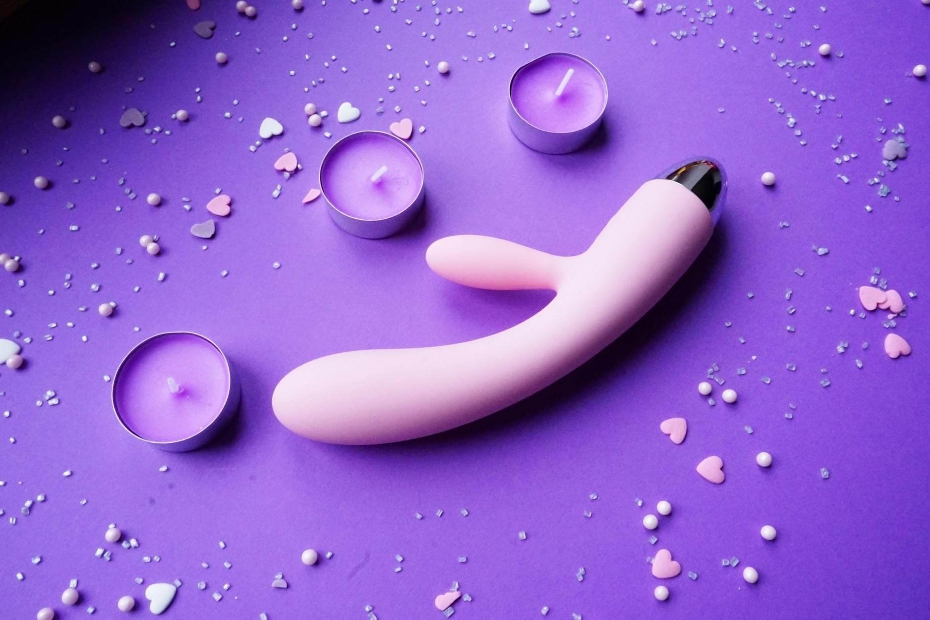 Rosa Zitronenvibrator auf violettem Hintergrund mit Herzkonfetti und Kerzen für romantische Atmosphäre