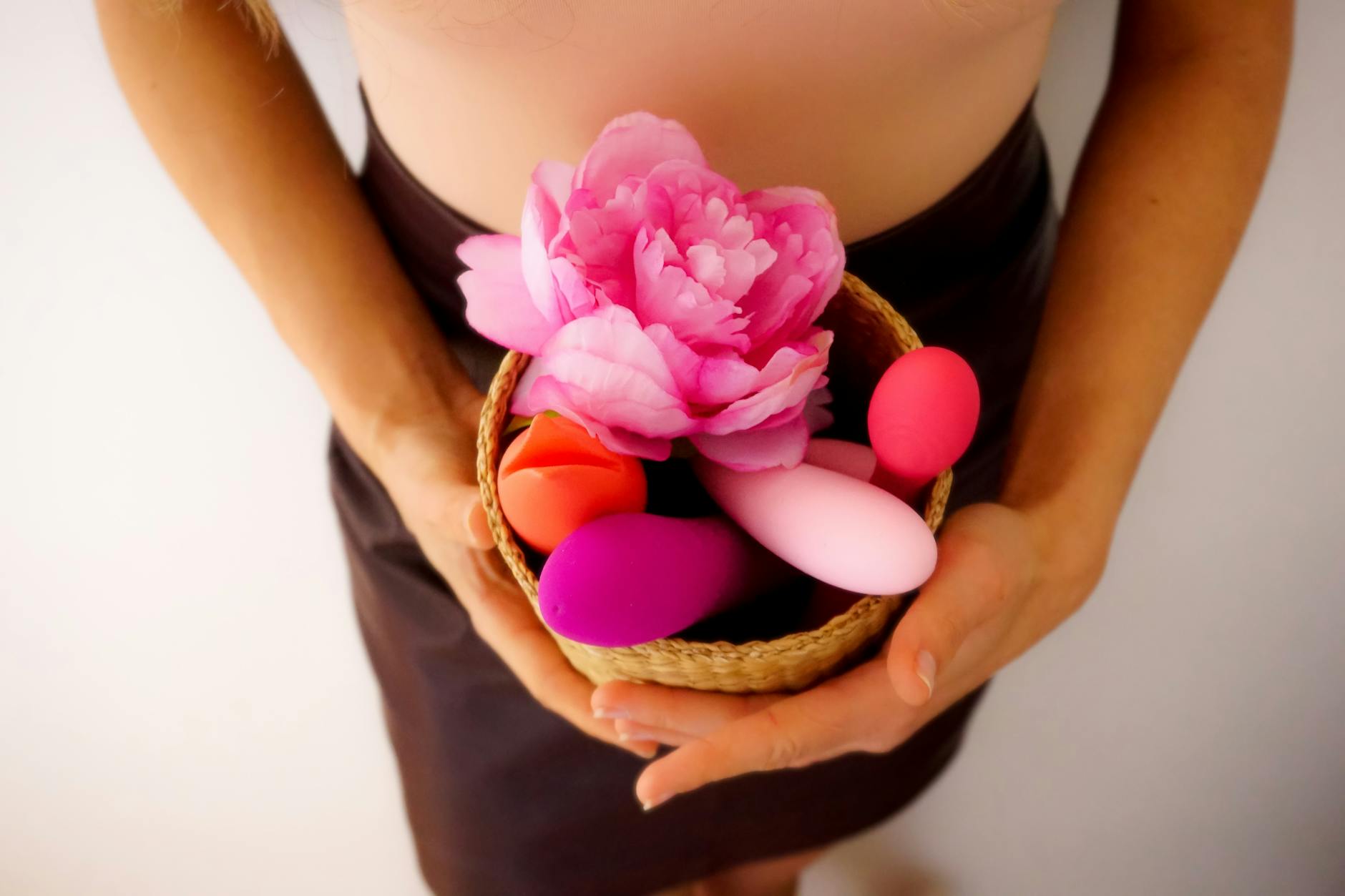 Eine Hand mit weißen Nägeln hält eine frische Zitrone auf zartem rosa Hintergrund, umgeben von drei weiteren Zitronen.